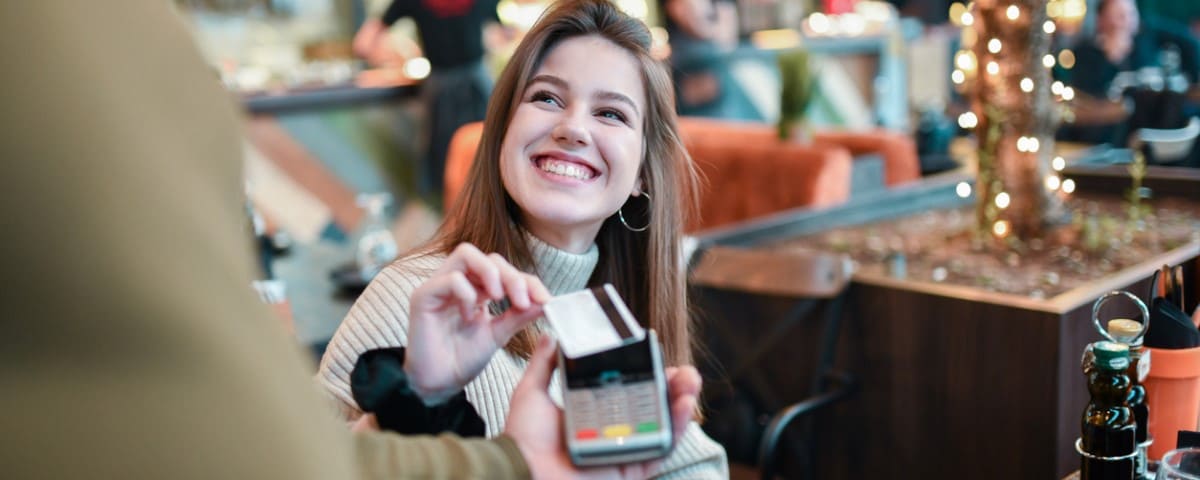 Femme souriante utilisant une carte de crédit pour un paiement sans contact dans un restaurant.