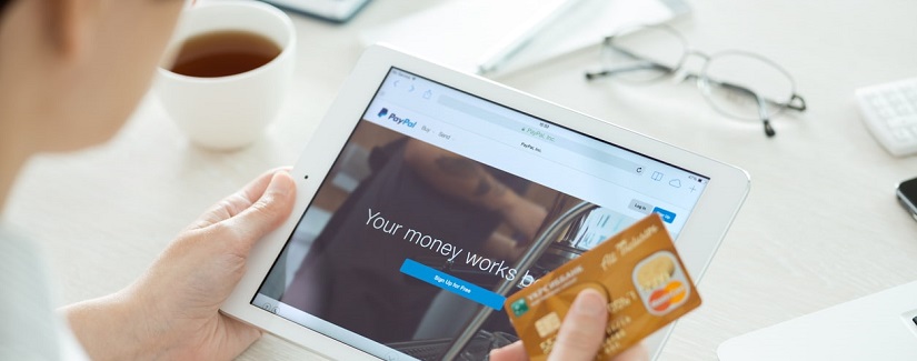 Personne avec carte de crédit en main à la recherche sur un tout nouveau Apple iPad Air avec le site Paypal sur un écran.
