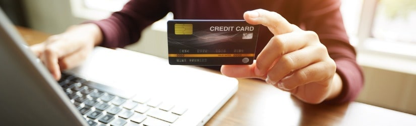 Mains tenant une carte de crédit en plastique et utilisant un ordinateur portable.