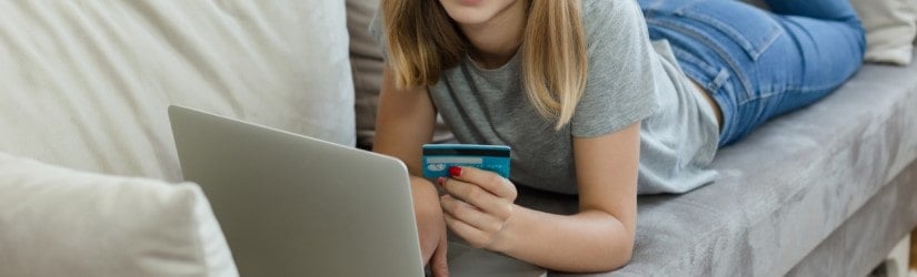 Une jeune femme blonde faisant du shopping en ligne sur un canapé.