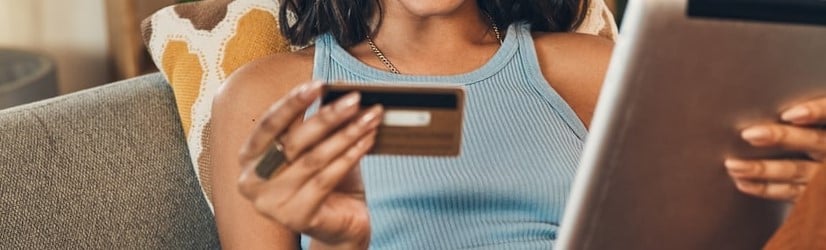 Femme métisse souriante utilisant une carte de crédit pour le commerce électronique sur une tablette numérique à la maison. 