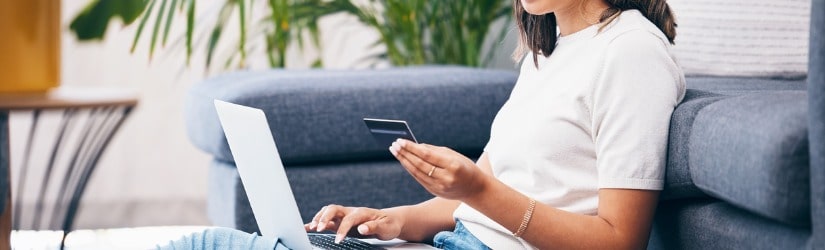 Jeune femme tenant un smartphone à l’aide d’un ordinateur portable pour faire visiter en ligne son état bancaire.